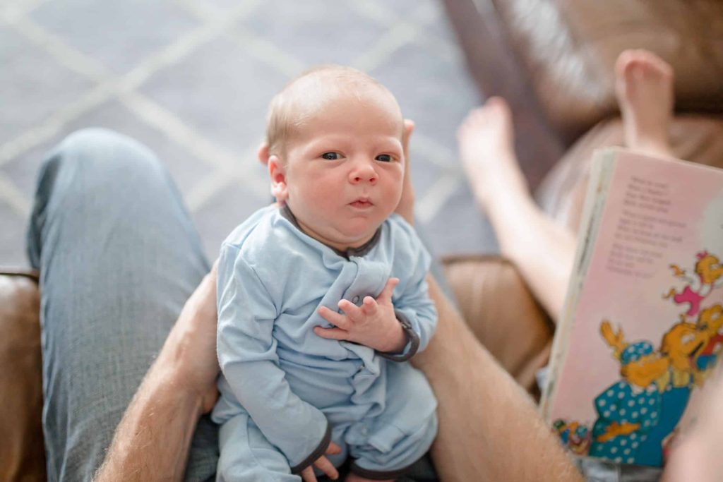 lifestyle newborn photographer baby boy looking into camera in dads arms