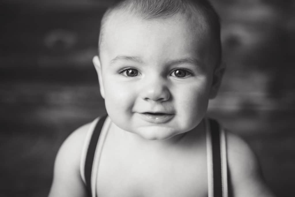 Cute 6 month old boy in suspenders smiling at the camera