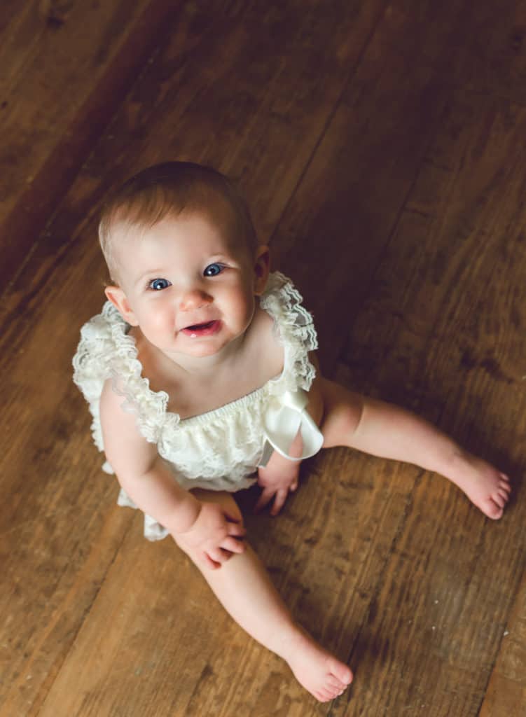 6 month old baby girl looking at the camera in white lace romper