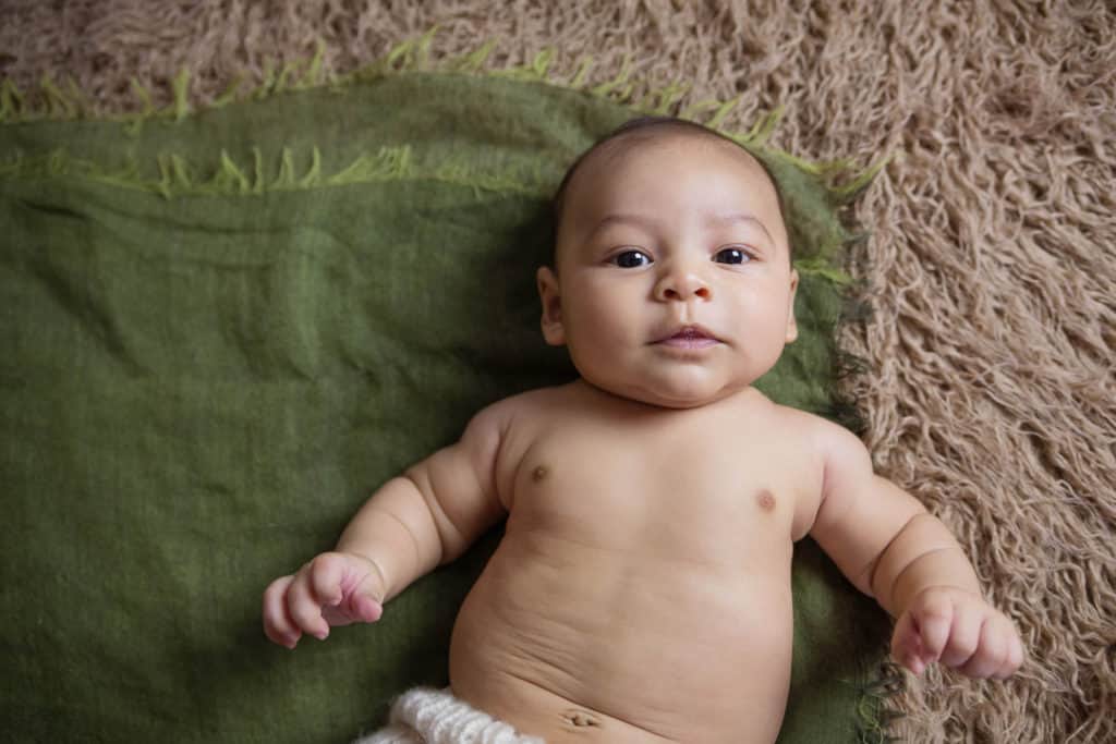 3 month old boy looking into the camera on a green blanket and tan flokati carpet