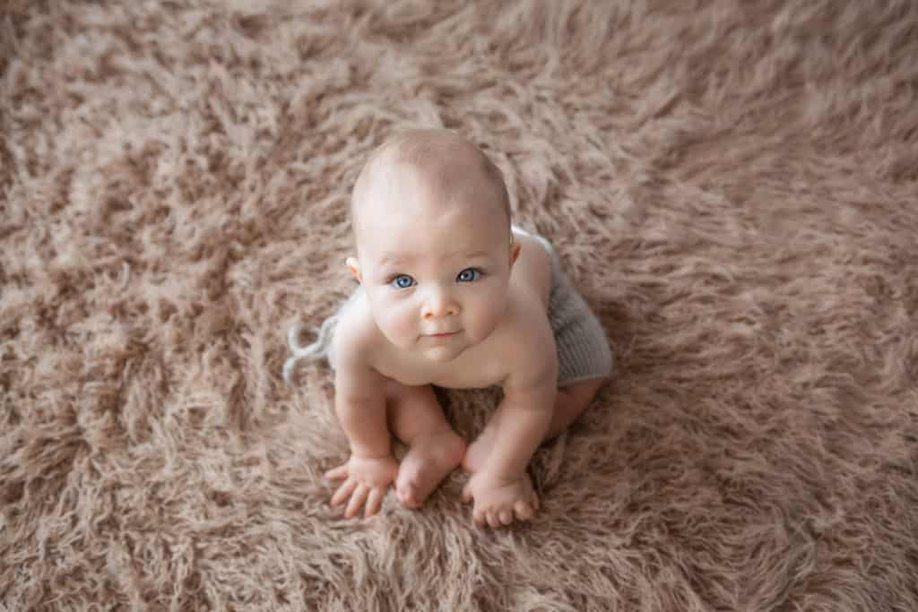 Baby boy 6 month old milestone shoot with looking at the camera dressed in neutrals