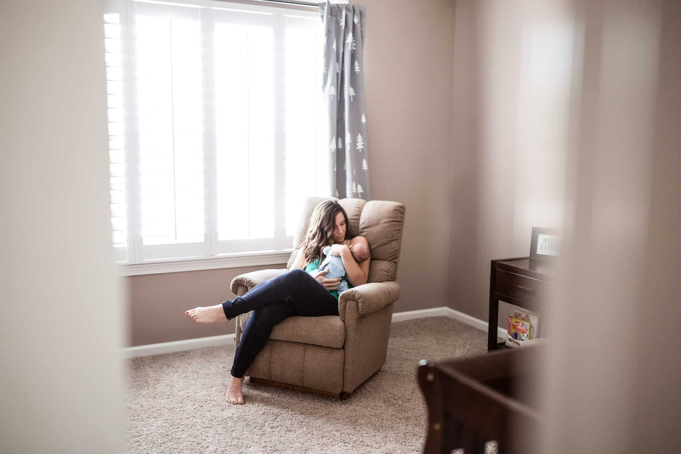 Mom and baby snuggling in nursery while Kansas City photographer peeking through the door while she rocks him