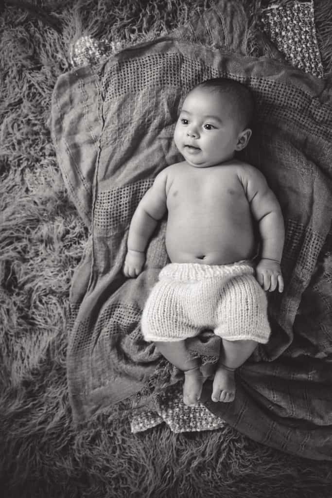 Cute hispanic baby boy laying on blankets and smiling in black and white image