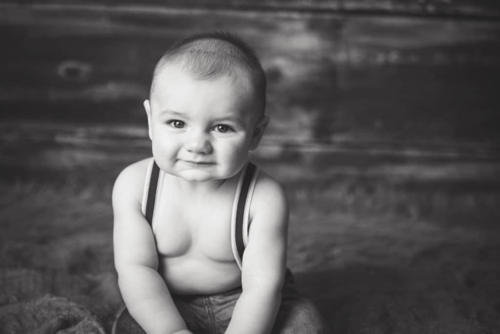 6 month old baby boy in suspenders smiling at camera
