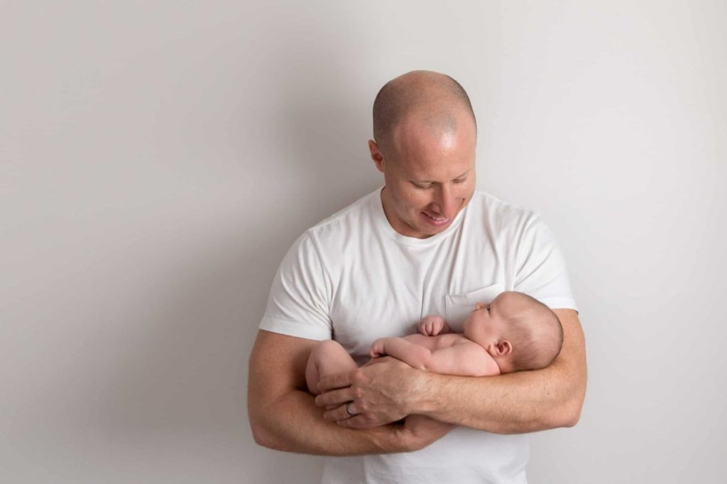 Kansas city newborn photographer dad holding baby girl and smiling